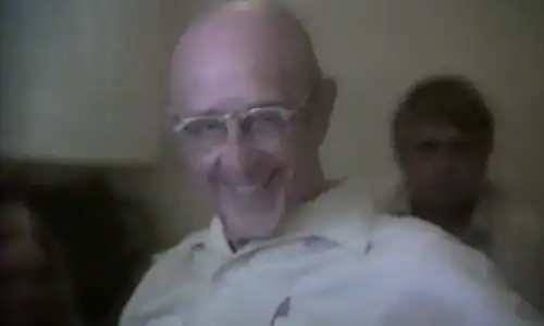 A bald man with glasses smiling in a kitchen.