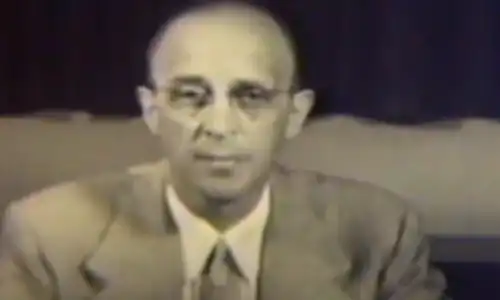 A man in a suit and tie is sitting in front of a television.