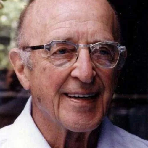 An older man wearing glasses and a white shirt.
